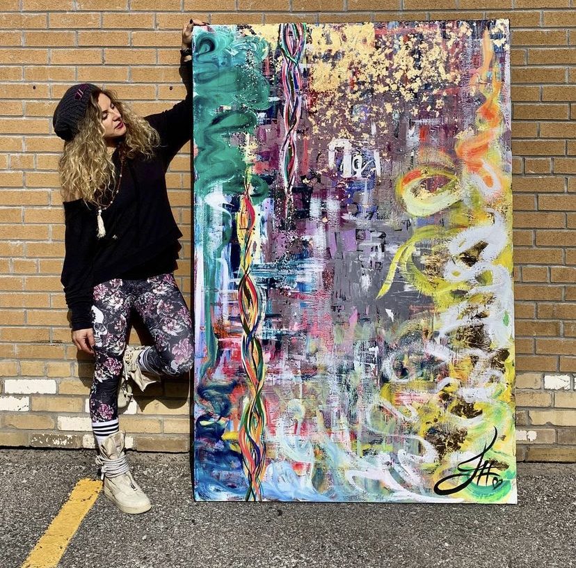 Jessica outdoors with a large mixed-media canvas against a brick wall