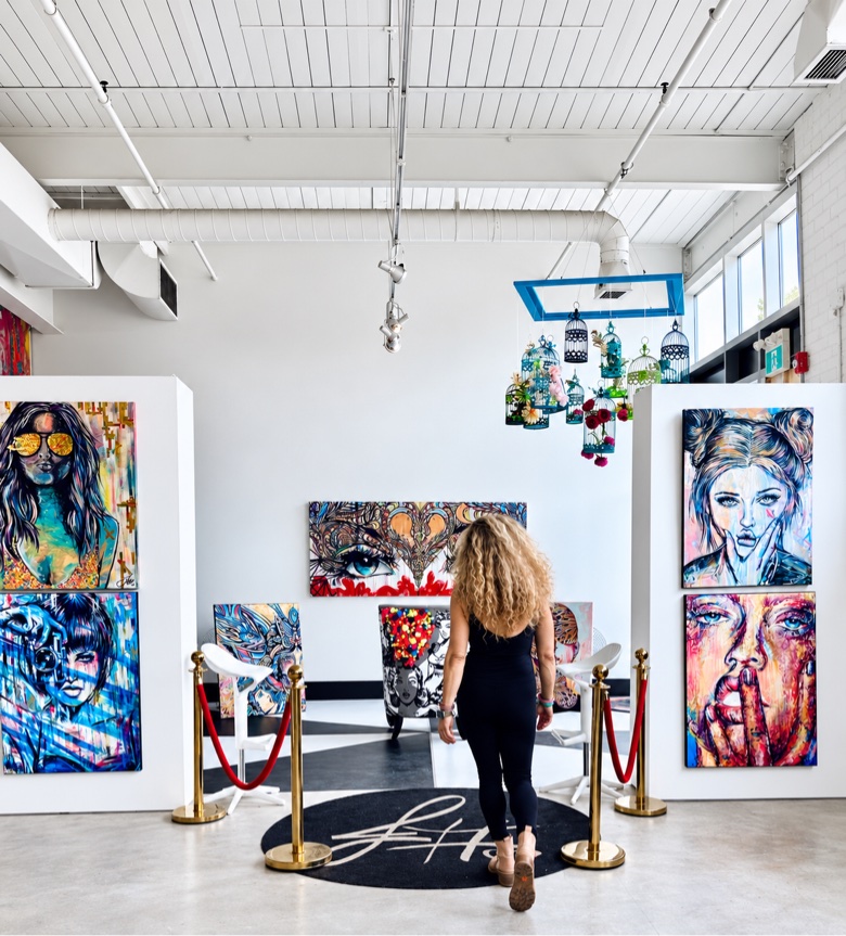 Jessica walking into her gallery past velvet ropes, pop portraits on the walls